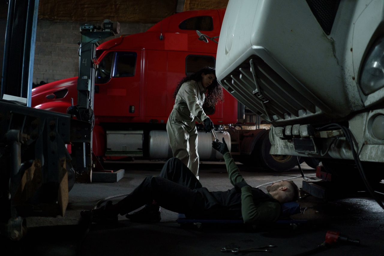 Two mechanics working together to repair a truck in a dimly lit garage setting.